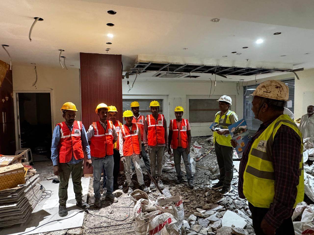 Site supervisor briefing workers in PPE kits — helmets and high-visibility vests — before starting work