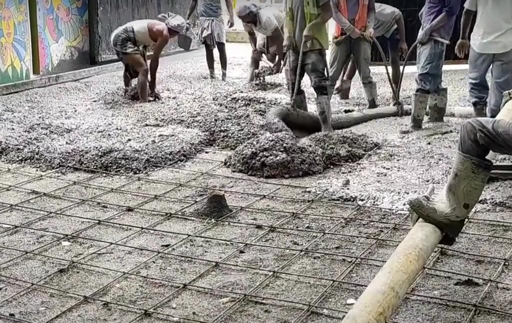 Workers laying RCC road over a rebar mesh grid